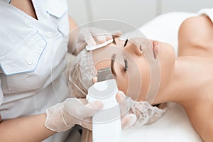 The doctor cleanses the woman`s skin with a special medical device. The woman came to procedure of laser hair removal.