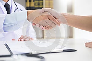 Doctor at the clinic giving an handshake to his patient for encouragement and empathy, healthcare and assistance concept