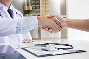 Doctor at the clinic giving an handshake to his patient for encouragement and empathy, healthcare and assistance concept