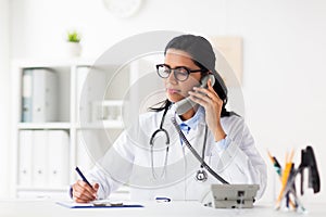 Doctor with clipboard calling on phone at hospital