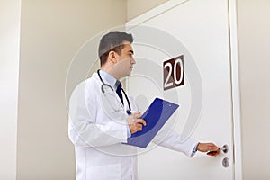 Doctor with clipboard opening hospital ward door