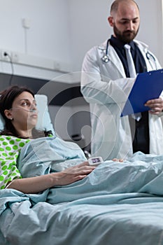 Doctor with clipboard reading medical data to patient with nasal cannula recieving oxygen