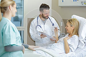 doctor with clipboard talks to woman in hospital bed