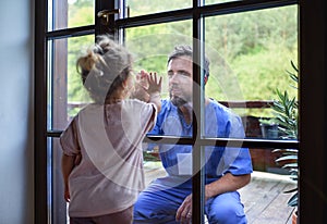 Doctor coming to see family in isolation, window glass separating them.