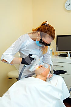 Doctor conducts procedure for rejuvenating facial skin with laser. Woman receiving facial beauty treatment, removing pigmentation