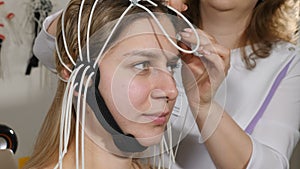 Doctor connecting electronic sensors with wires to female patient. Young woman wired to EEG machine or