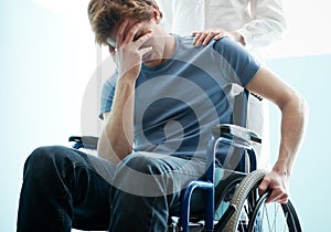 Doctor consoling young man sitting in wheelchair