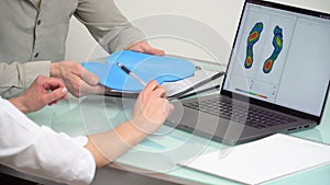 Doctor consulting male patient on custom orthotic insoles in a clinic for a personalised custom fitusing test picture on a laptop