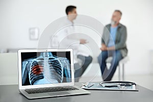 Doctor consulting man in clinic. Focus on laptop displaying x-ray of patient with lung cancer