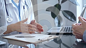 Doctor consulting patient in clinic office while both are sitting at the glass desk. Medicine concept