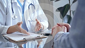 Doctor consulting patient in clinic office while both are sitting at the glass desk. Medicine concept