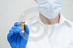 Doctor cosmetician in mask keeps in his hand in blue gloves ampoule with drug