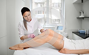 Doctor-cosmetician performs a cosmetic procedure on the patient`s legs with electronic medical device in beauty parlor