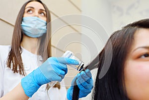 doctor cosmetologist dermatologist diagnoses the condition of the patient& x27;s hair using a special device - a