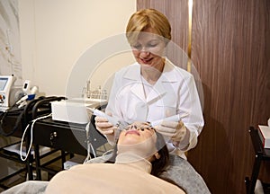 Doctor cosmetologist doing a professional treatment for facial muscle stimulation to regain tone on the face of a young woman.