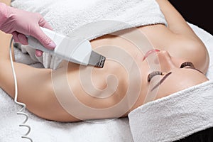 The doctor-cosmetologist makes the apparatus a procedure of ultrasound cleaning of the decollete skin of a beautiful, young woman photo