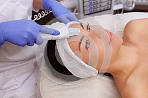 The doctor-cosmetologist makes the apparatus a procedure of ultrasound cleaning of the facial skin of a beautiful, young woman in