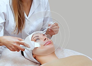 The doctor-cosmetologist makes the apparatus a procedure of ultrasound cleaning of the facial skin of a beautiful, young woman