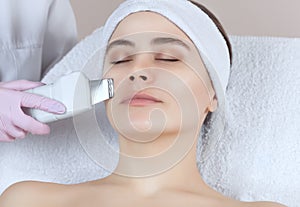 The doctor-cosmetologist makes the apparatus a procedure of ultrasound cleaning of the facial skin of a beautiful, young woman in