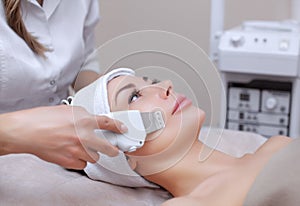 The doctor-cosmetologist makes the apparatus a procedure of ultrasound cleaning of the facial skin of a beautiful, young woman