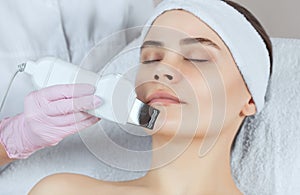 The doctor-cosmetologist makes the apparatus a procedure of ultrasound cleaning of the facial skin of a beautiful, young woman in