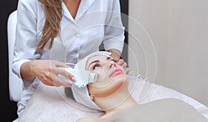 The doctor-cosmetologist makes the apparatus a procedure of ultrasound cleaning of the facial skin of a beautiful, young woman