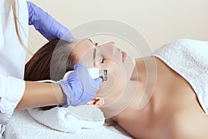The doctor-cosmetologist makes the apparatus ultrasound cleaning procedure of of the facial skin of a beautiful young woman in a