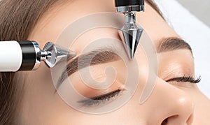 A doctor cosmetologist makes a microcurrent facial therapy to a young woman with a device in a beauty wellness salon.Cosmetology