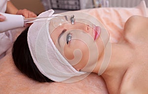 The doctor-cosmetologist makes the procedure Microcurrent therapy of the facial skin on the forehead