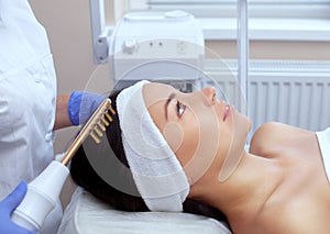 The doctor-cosmetologist makes the procedure Microcurrent therapy On the hair of a beautiful, young woman in a beauty salon.