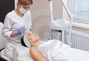 The doctor-cosmetologist makes the procedure treatment of Couperose of the facial skin of a beautiful, young woman