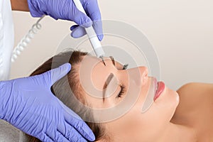 The doctor-cosmetologist makes the procedure treatment of Couperose of the facial skin of a beautiful, young woman in a beauty photo
