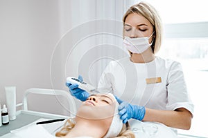 Doctor cosmetologist makes professional cleansing of the woman facial skin using scrubber.