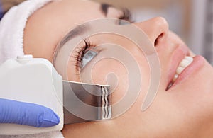 The doctor-cosmetologist makes the ultrasound cleaning procedure of the facial skin of a beautiful, young woman