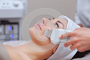 The doctor-cosmetologist makes the ultrasound cleaning procedure of the facial skin of a beautiful, young woman in a beauty salon.