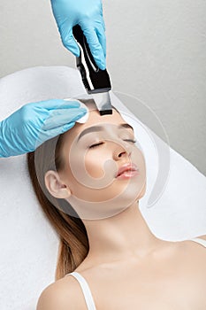 The doctor-cosmetologist makes the ultrasound cleaning procedure of the facial skin of a beautiful, young woman in a beauty salon