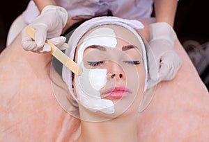 The doctor is a cosmetologist for the procedure of cleansing and moisturizing the skin, applying a mask with stick to the face