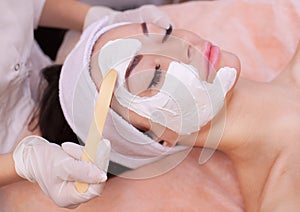 The doctor is a cosmetologist for the procedure of cleansing and moisturizing the skin, applying a mask with stick to the face of