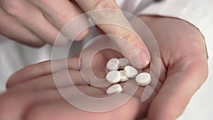 A doctor is counting white pills on his hand in close-up