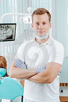 Doctor dentist smiling and standing with hands crossed in dental clinic on backdrop with medical equipment, x-ray dental and