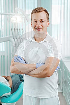Doctor dentist smiling and standing with hands crossed in dental clinic on backdrop with medical equipment, x-ray dental and