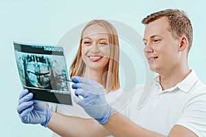 Doctor dentist and woman patient watching x-ray foto with teeth in in light blue background in dental clinic. Smile healthy teeth