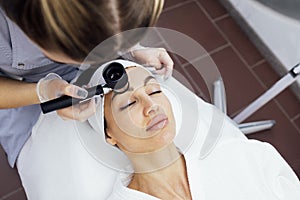 Doctor dermatologist examines skin of client face of beauty salon with a dermatological lens photo