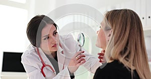 Doctor dermatologist examining patient facial skin with magnifying glass in clinic 4k movie slow motion