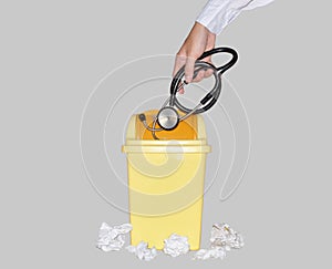 Doctor discarding Stethoscope into Small Yellow Plastic Trash Can. Shows Quit the Medical Job, Disappoint and Give up Doctor