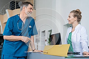 Doctor In Discussion With Nurse At Nurses Station or Hospital Reception.