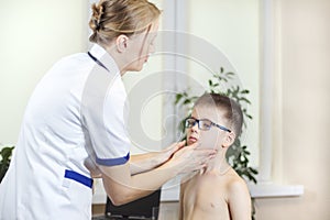 Doctor in a doctor`s office while medical examining the tonsils of a boy with glasses.