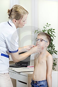 Doctor in a doctor`s office while medical examining the tonsils of a boy with glasses.