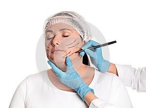 Doctor drawing marks on woman`s face for cosmetic surgery operation against background. Double chin problem