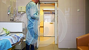 A doctor in a dressing gown opens an automatic door in the patient`s room